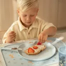 Kisfiú gyümölccsel díszíti az uzsonnát a Little Dutch tányéralátét felett