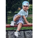 Kisgyermek kék színű Makaszka napellenzős bambusz sapkában a szabadban egy padon ülve
