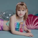 Kislány sellő jelmezben fekszik a Petit Boum Sea Sparkle Move Bottle mellett mosolyogva kék háttér előtt