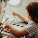 Kisgyermek rajzol a Kidywolf Mini LCD rajztáblára a repülőgép asztalán a mellékelt állatos sablon kíséretében