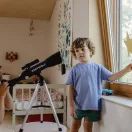 Gyermek a szobában az ablak felé irányított Kidywolf csillagászati távcsővel