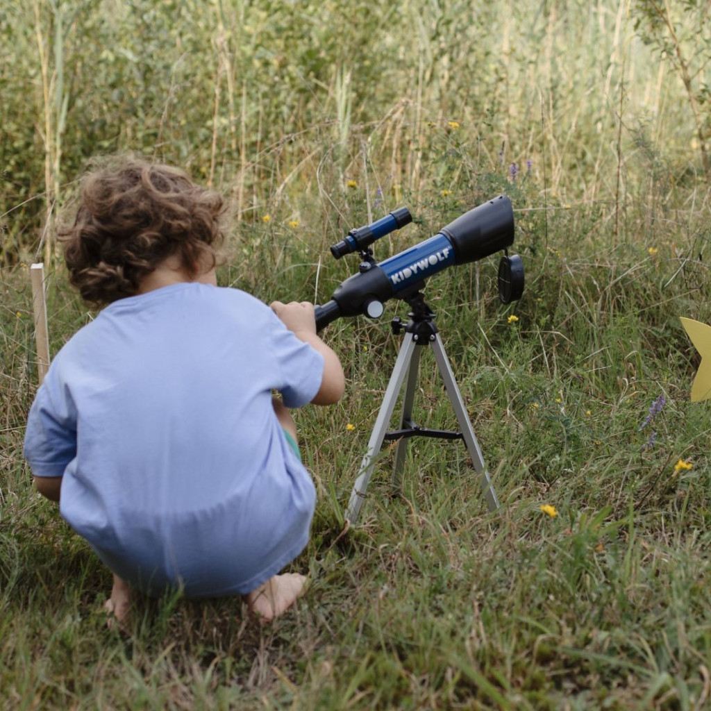 Gyerek a Kidywolf Kidytelescope csillagászati távcsővel a réten, a KIDYWOLF felirat jól látható a csövön
