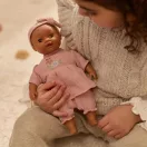 Tipegő gyermek ölében ül a rózsaszín ruhás Little Dutch Yara baba
