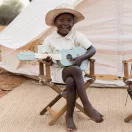 Kisfiú játszik a Little Dutch Safari Friends fa gitárral egy sátor előtt